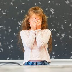 Mädchen steht vor einer Tafel - Buchstaben schweben um sie herum